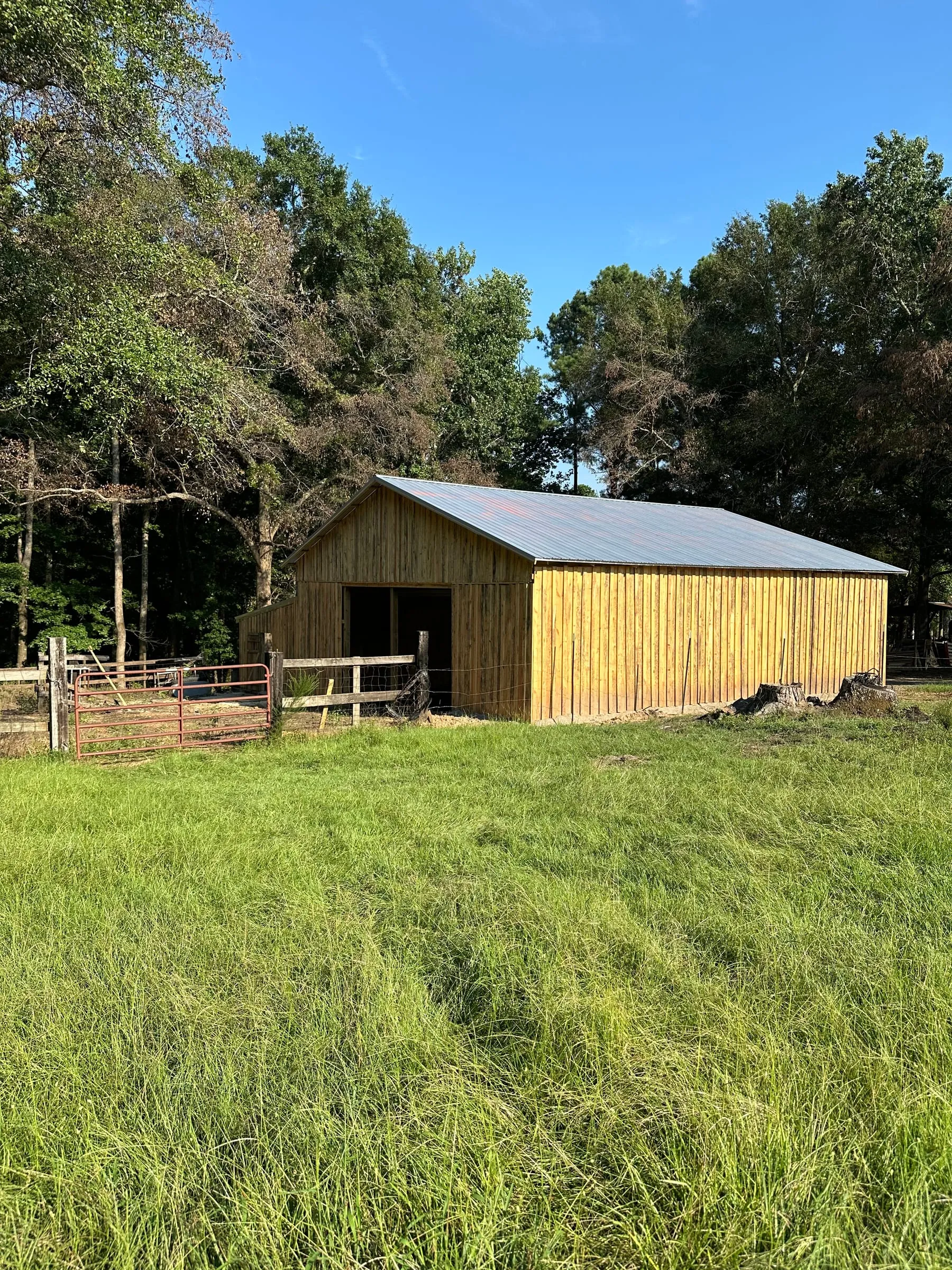 Finished pole barn with rough-cut vertical board siding and a galvanized metal roof, seen across a grass pasture.