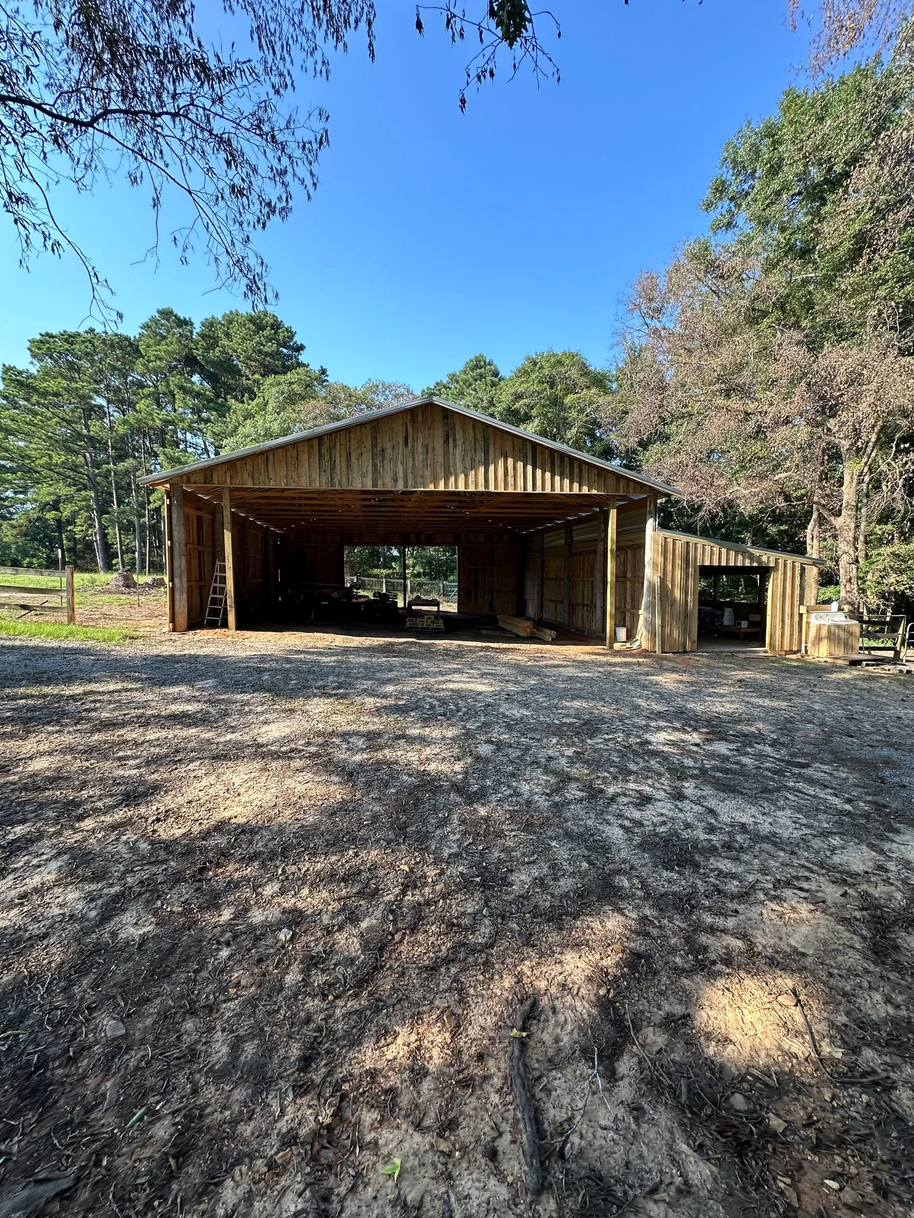 Gable end of the board-sided pole barn with an open bay and a red pipe gate.