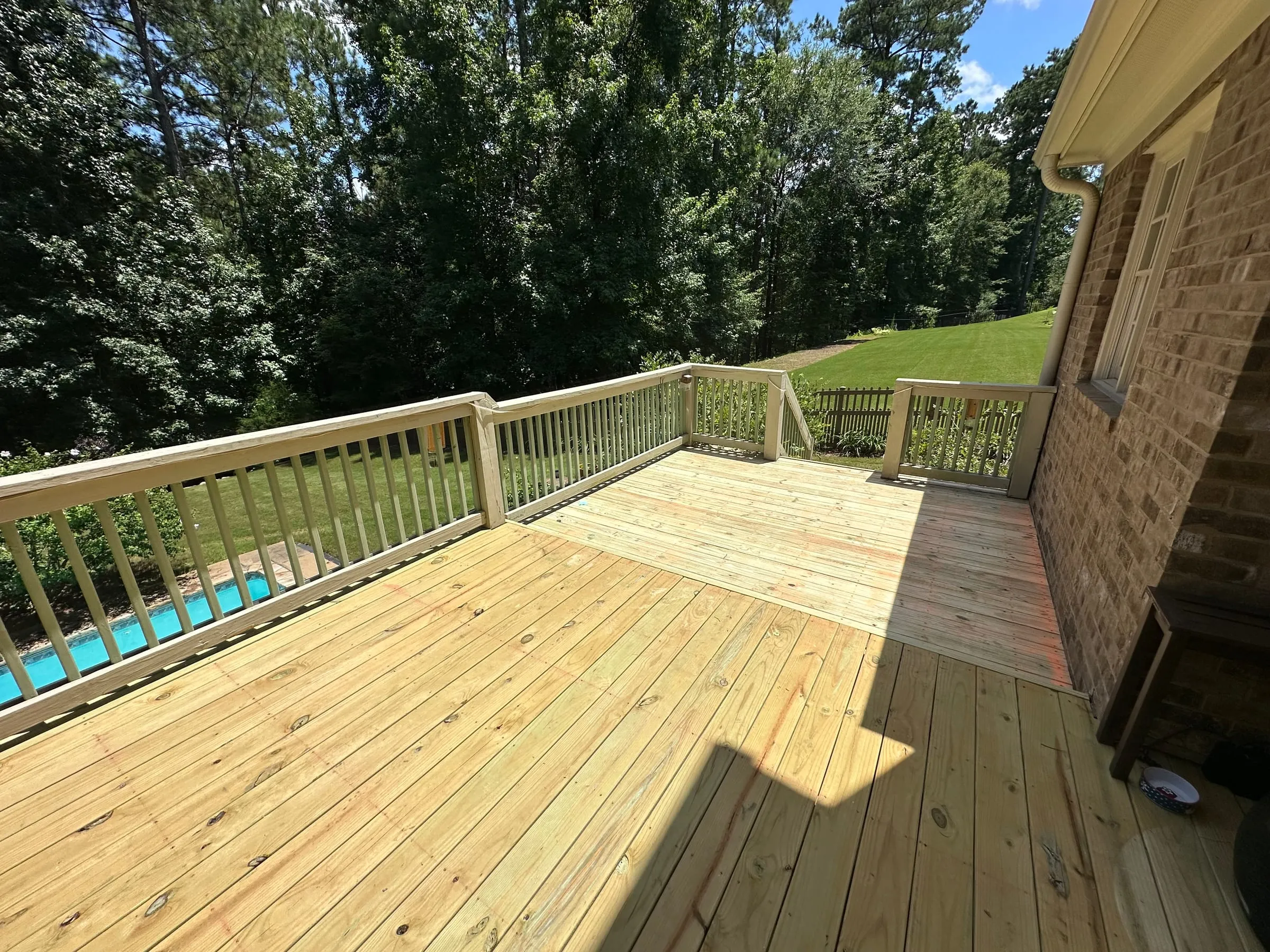 Deck rail overlooking the backyard pool and tree line, fresh pressure-treated boards in the foreground.